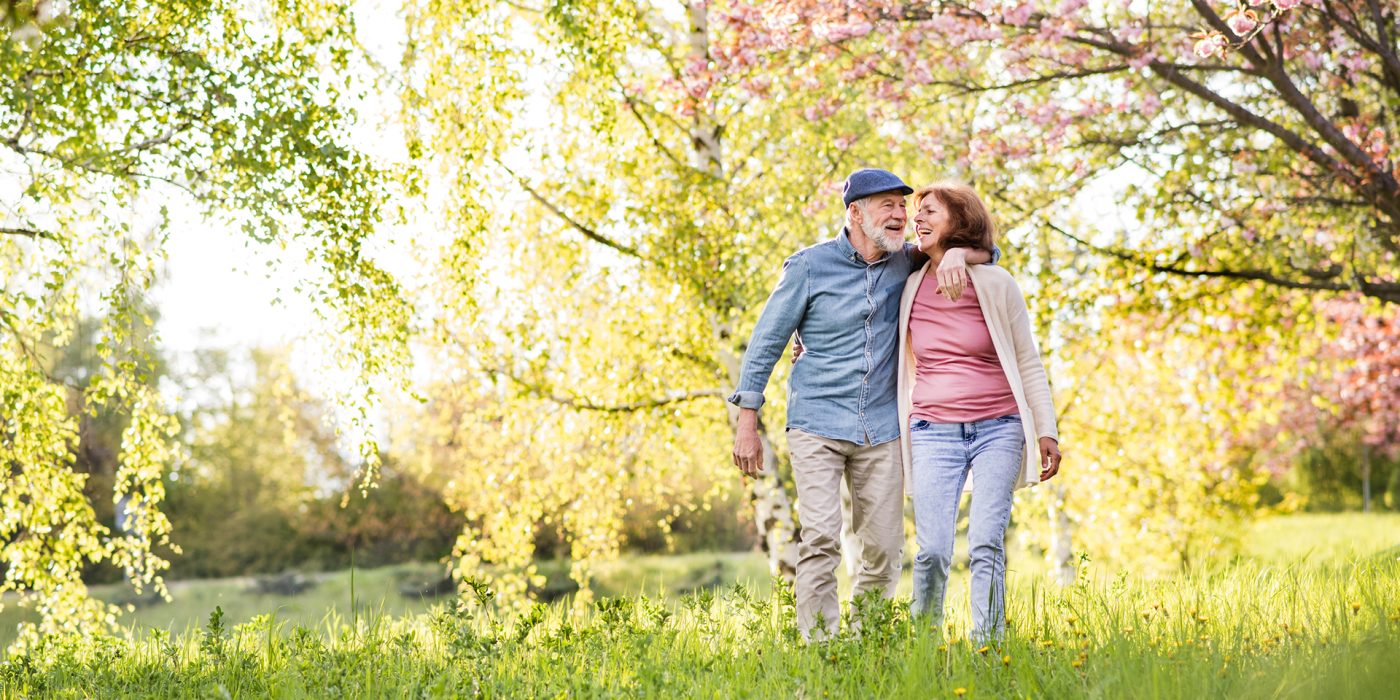 Beautiful senior couple in love on a walk outside in spring nature under blossoming trees.