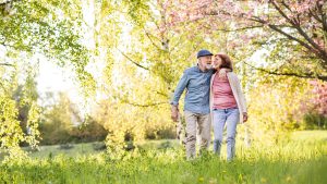 Beautiful senior couple in love on a walk outside in spring nature under blossoming trees.